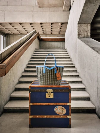 Tan patterned tote bag with blue trim sitting on top of a blue trunk, photographed in a concrete stairwell with natural lighting.