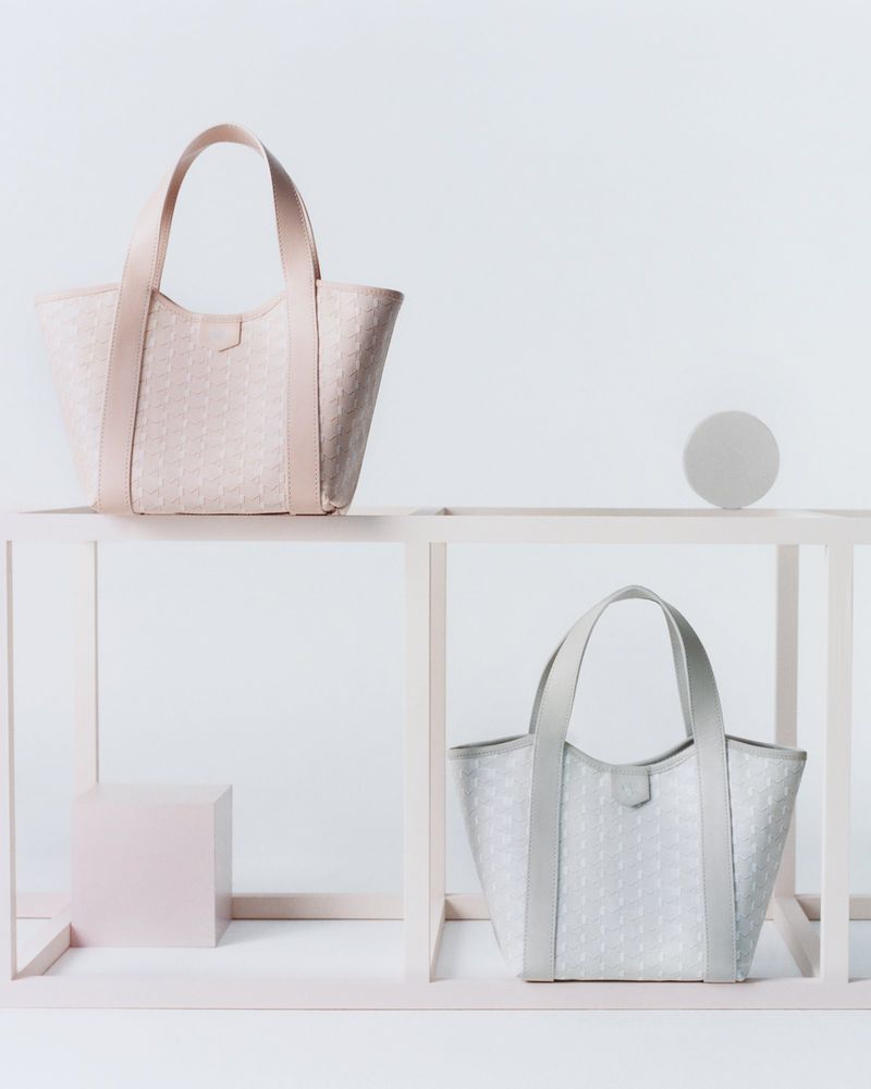Two patterned tote bags, one pink and one gray, are displayed on a modern pink and white shelf against a white backdrop.