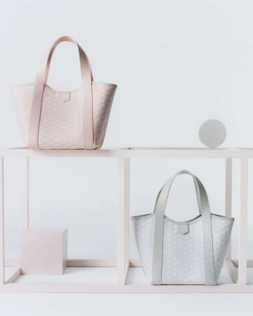 Two patterned tote bags, one pink and one gray, are displayed on a modern pink and white shelf against a white backdrop.