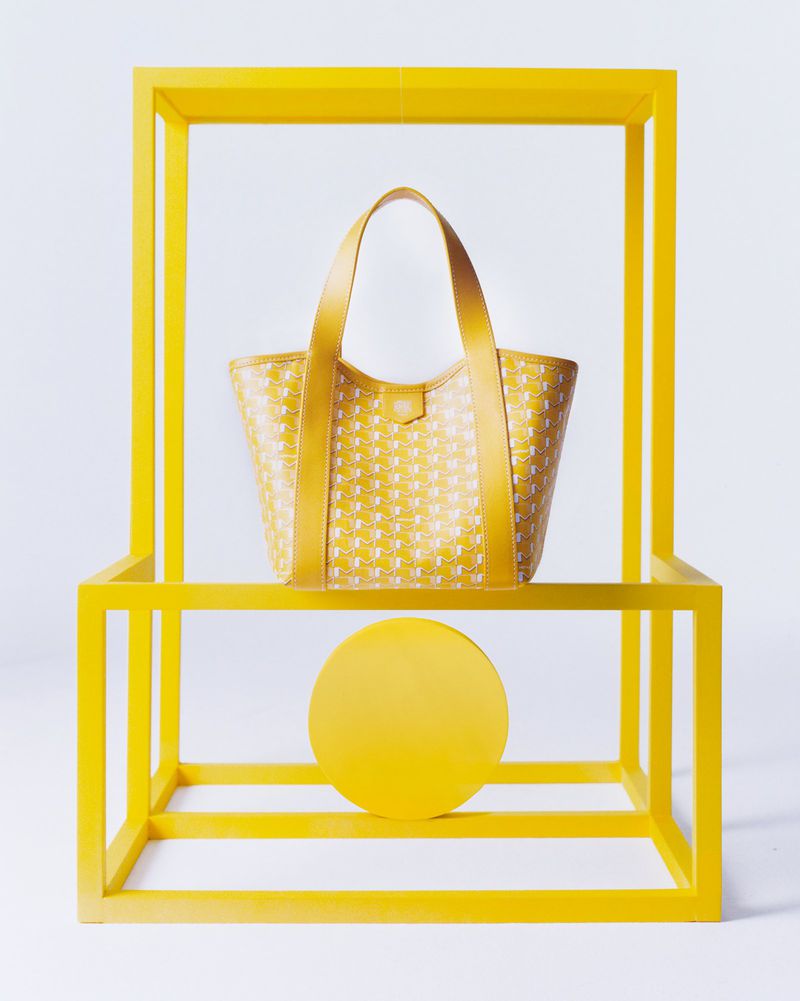 Fashion still life shot of a yellow patterned tote bag centered in a yellow display frame against a white background.