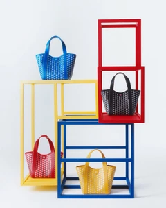 Four colorful Moynat Duo BB Canvas tote bags displayed within primary-colored geometric wooden cube frames against a white background.