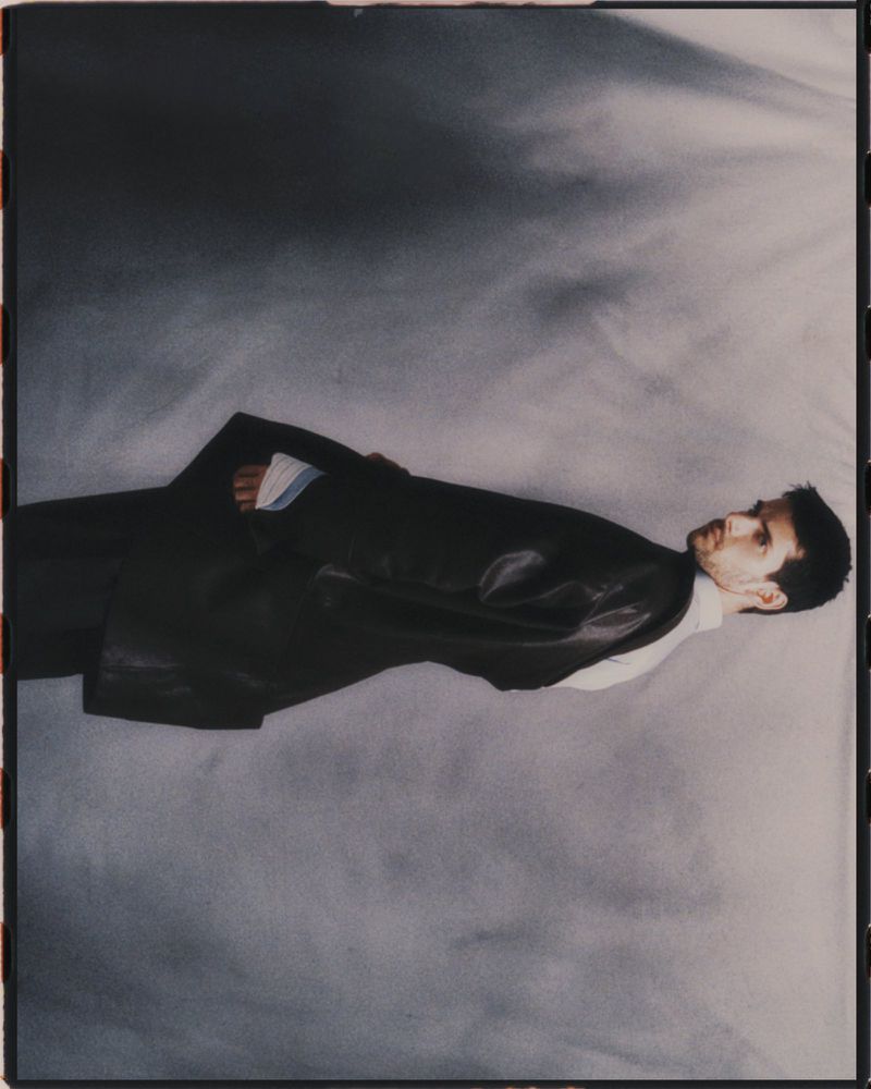 Portrait of a man in a suit jacket lying against a grey backdrop in an artistic style, showcasing a modern fashion aesthetic.