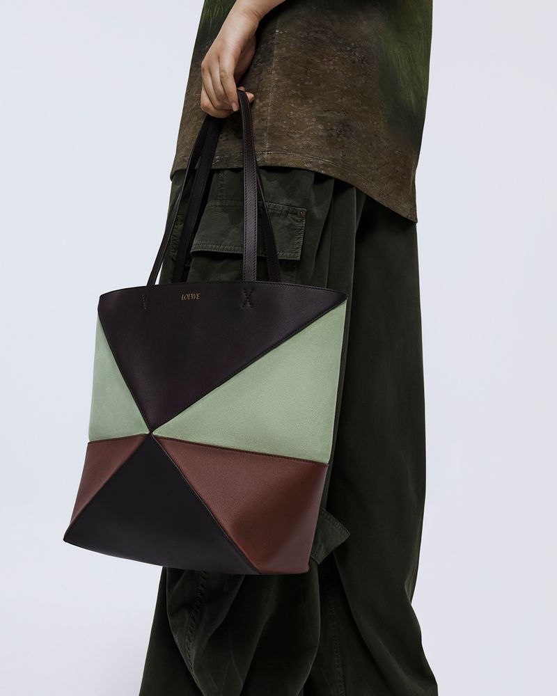 Geometric tote bag with brown, black, and green panels held by an adult. Fashion product shot with neutral background.