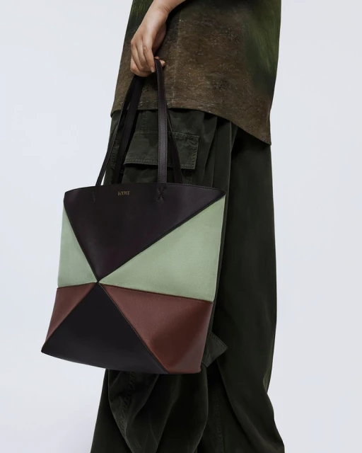 Geometric tote bag with brown, black, and green panels held by an adult. Fashion product shot with neutral background.