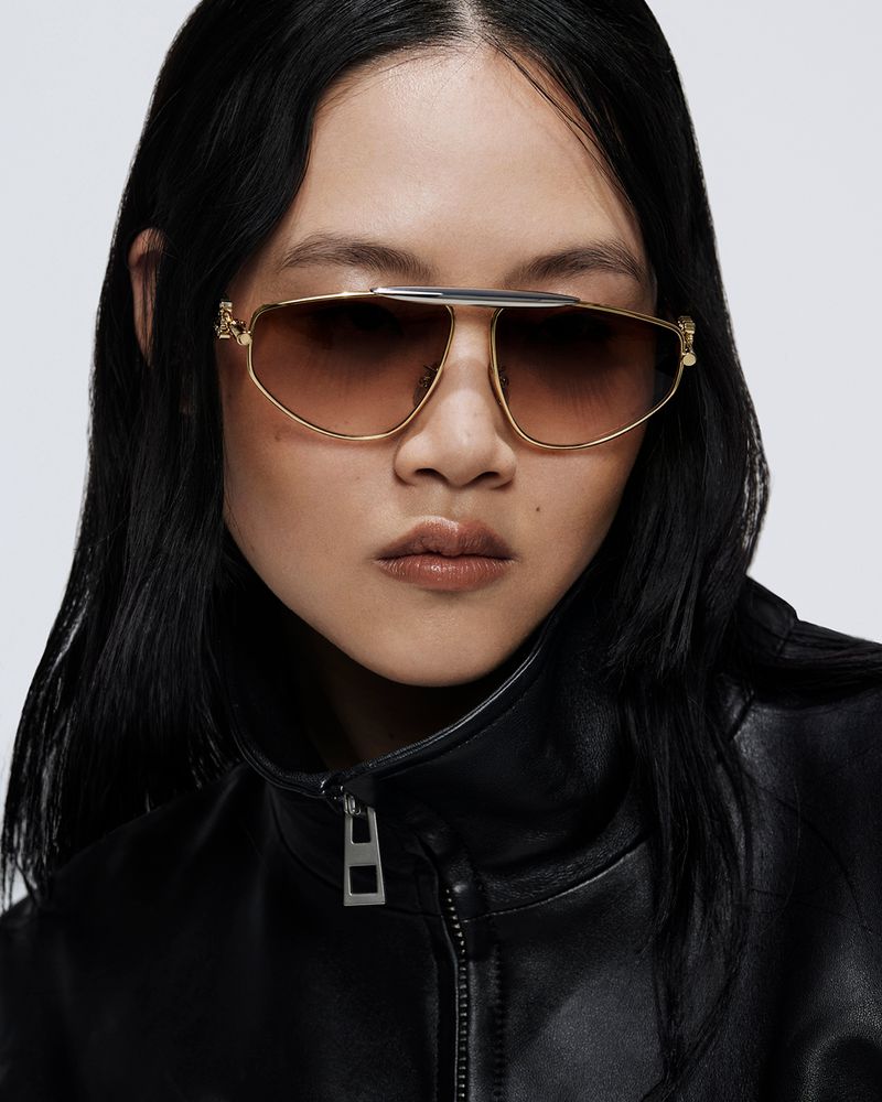 Portrait of a woman wearing aviator sunglasses and a black leather jacket against a neutral background in a studio setting.