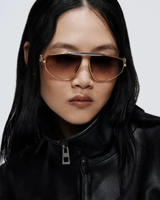 Portrait of a woman wearing aviator sunglasses and a black leather jacket against a neutral background in a studio setting.