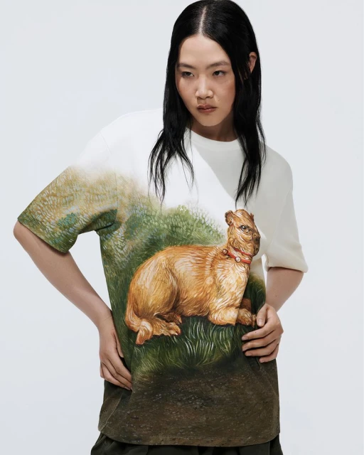 A young adult woman wears a printed t-shirt with a capybara design against a neutral backdrop in a medium studio shot.