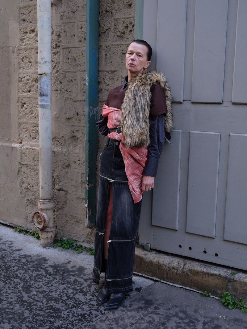Adult female poses in an outdoor urban setting wearing a skirt with zippers, a faux fur stole, and heeled boots, showcasing fashion.