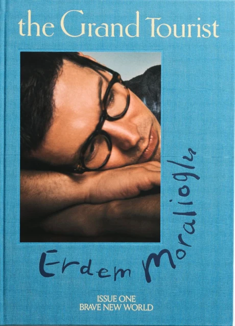 Magazine cover featuring a close-up of a man with glasses resting his head on his arms, with the title 'The Grand Tourist'.