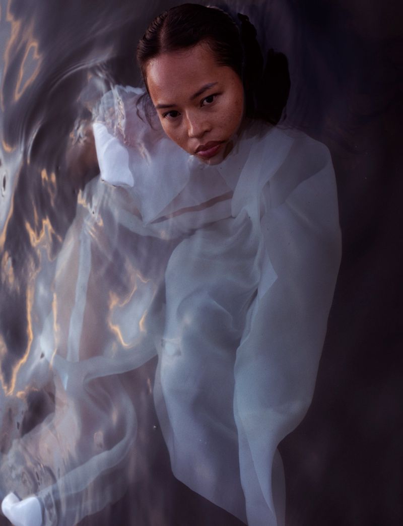 Woman in water wearing a white dress looking directly at the camera. Dark hair, fair skin, and soft natural light.