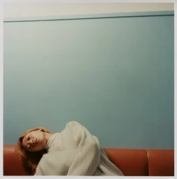 Woman in a light-coloured knitted sweater reclining on a brown leather sofa against a blue wall