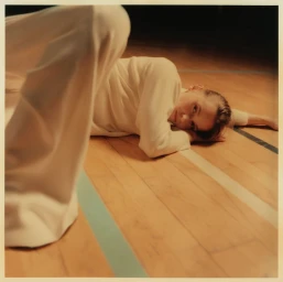 Model wearing cream long-sleeve top and trousers lying on wooden floor with painted court lines