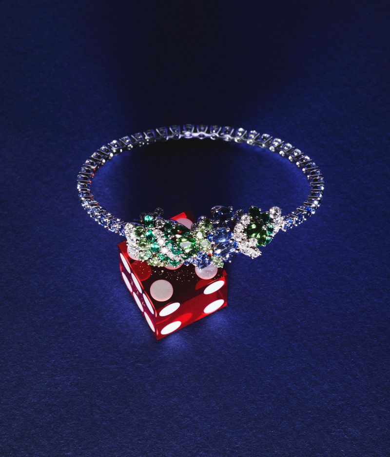 Close-up of a diamond and gemstone bracelet atop a red die, showcasing jewellery and gaming elements against a blue background.