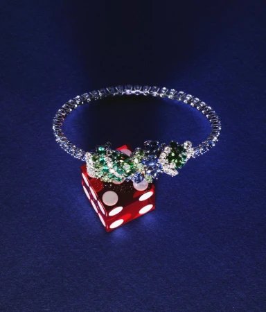 Close-up of a diamond and gemstone bracelet atop a red die, showcasing jewellery and gaming elements against a blue background.