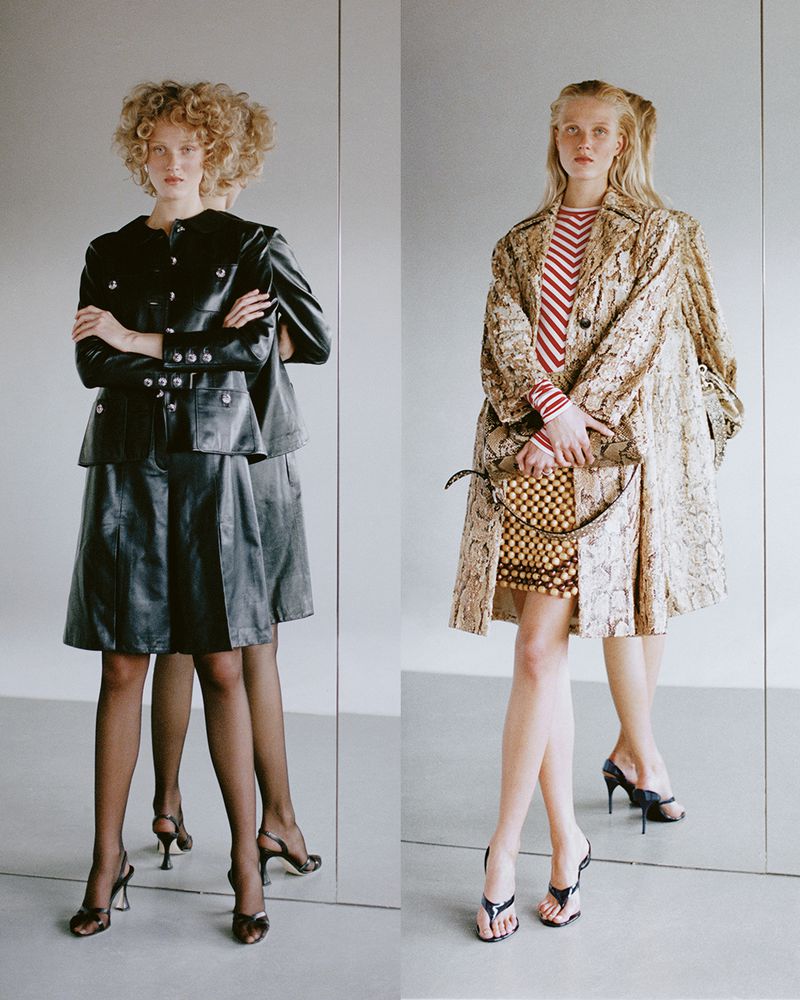 Two women in stylish patterned jackets and black heels pose in front of a reflective wall for a fashion studio shot.