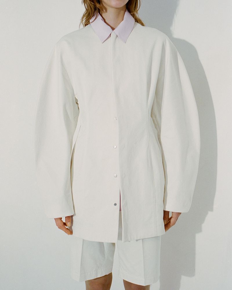 Fashion shot of a woman wearing an oversized off-white button-down shirt and matching shorts against a neutral background.