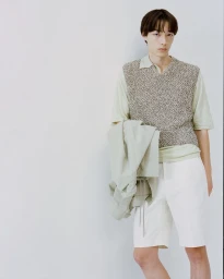 Young man in a textured knit vest holding a light jacket against a white background for Auralee Chino Days