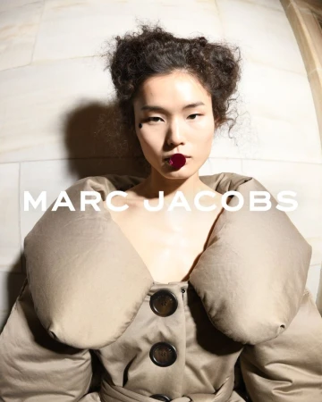 Asian fashion model poses indoors wearing a tan trench coat with a button-up front for Marc Jacobs brand advertising campaign.