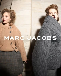 Two models wearing textured knitwear and patterned skirts standing against a marble pillar for Marc Jacobs