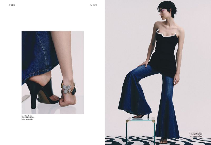 A young adult female poses in a fashion editorial image wearing a black strapless top and wide-leg denim jeans in a photo studio.