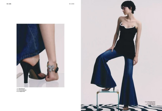 A young adult female poses in a fashion editorial image wearing a black strapless top and wide-leg denim jeans in a photo studio.