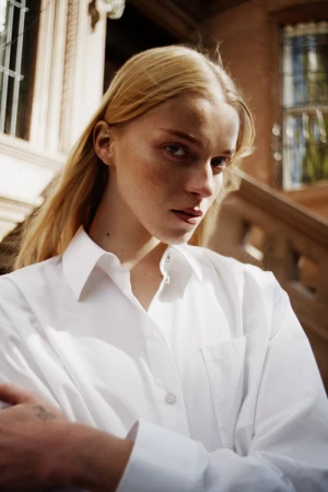 Model with blonde hair wearing a crisp white collared shirt outdoors against a building exterior background