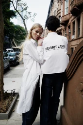 Two models wearing white shirts and dark trousers outdoors on a city street for Helmut Lang Resort 25