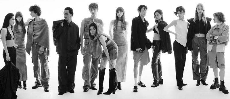 Group of fashion models in an indoor studio, posing in a diverse range of modern monochrome clothing against a bright white background.
