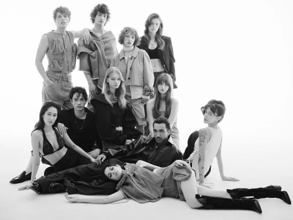 Black and white studio shot of a diverse group of fashion models posing together, wearing various clothing styles and standing on a white backdrop.
