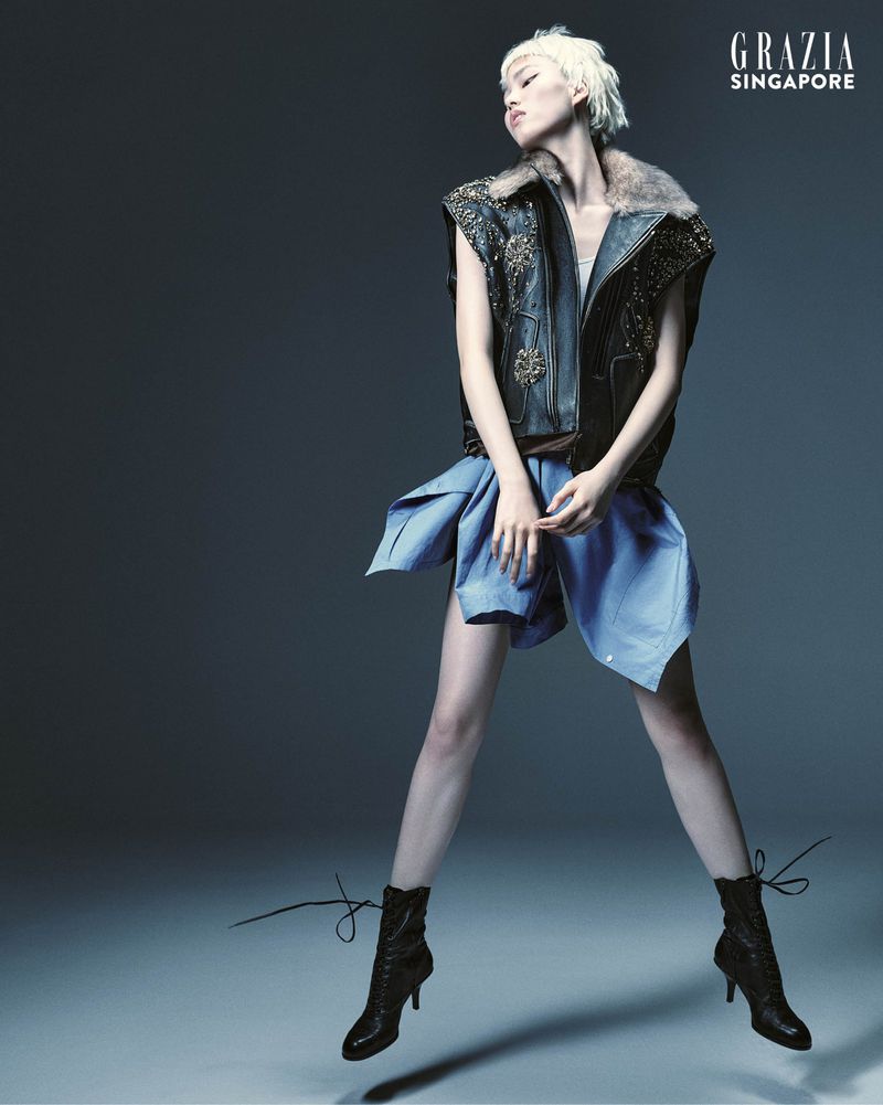 Fashion editorial shot of a woman in a blue dress and vest standing on a blueish-gray background, shot for Grazia Singapore.
