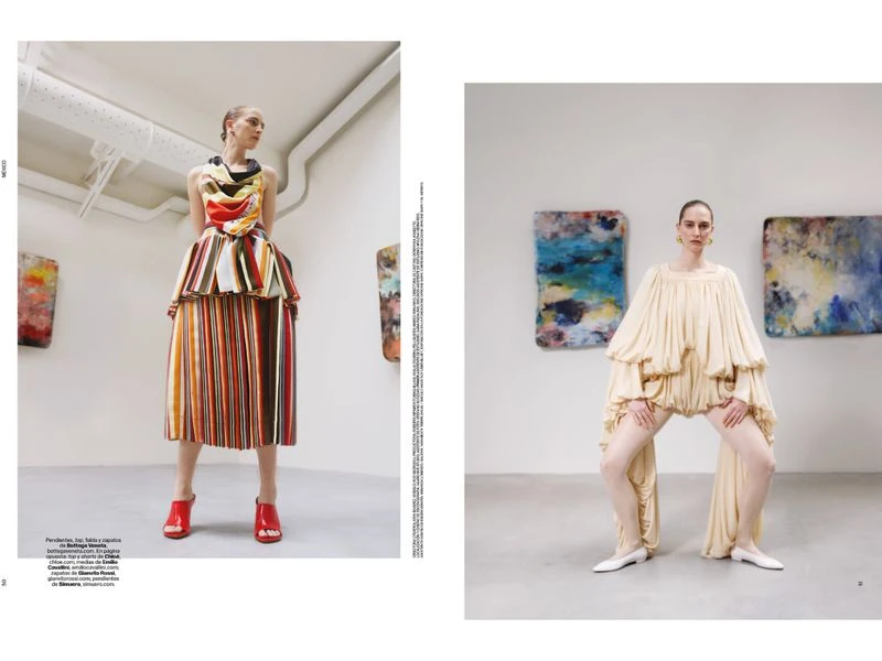 Fashion editorial featuring two women in colorful, voluminous clothing posing in a minimalist white art gallery with abstract paintings.