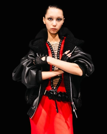 Portrait of a woman with crossed arms wearing a red dress and black leather jacket in a studio with a black background.