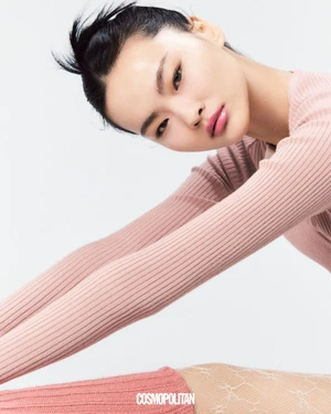 East Asian woman in pink ribbed long-sleeve top stretching against a clean white background with Cosmopolitan logo