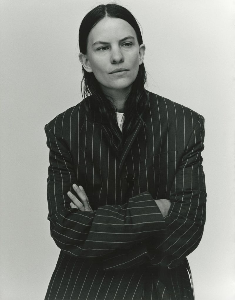 Striking black and white portrait of an adult woman wearing a pinstripe blazer with her arms crossed, captured in a photo studio.