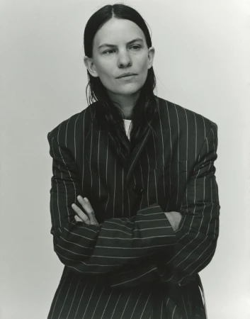 Striking black and white portrait of an adult woman wearing a pinstripe blazer with her arms crossed, captured in a photo studio.