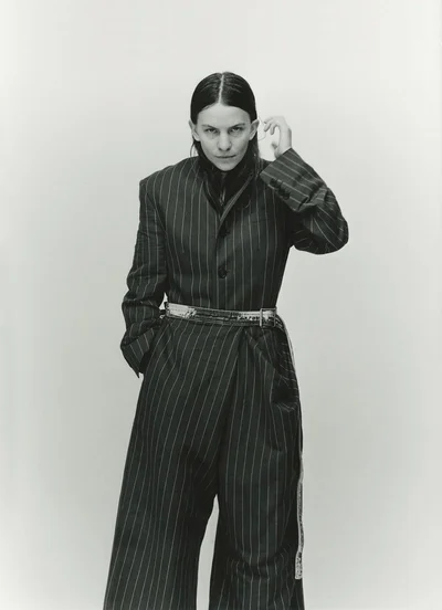 Model wearing a pinstripe suit and patterned belt against a plain grey studio backdrop