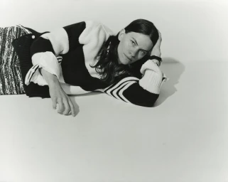 Eliot Sumner reclining on a light studio floor wearing a black and white striped knit sweater and textured patterned trousers.