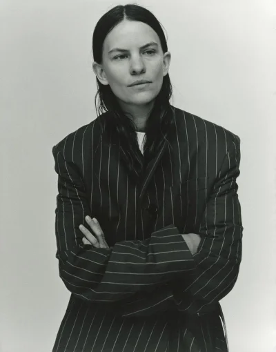 Eliot Sumner wearing an oversized pinstripe blazer with arms crossed against a seamless studio background.