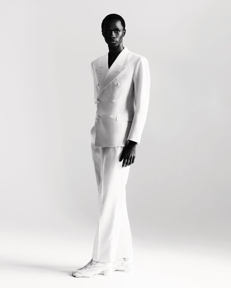 Black male model in a white double-breasted suit posing in a studio setting with white background. Fashion editorial photography.