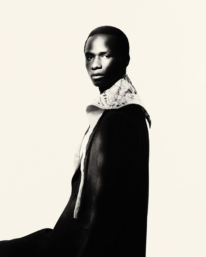 Model Malick Bodian in a black coat with a wide patterned collar posing against an off-white background.