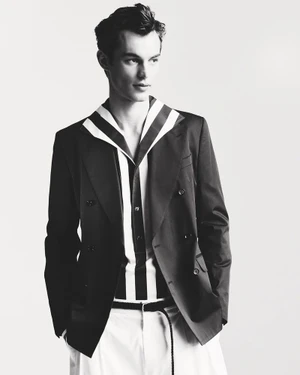 Portrait of a male model wearing a dark double-breasted blazer and striped shirt against a plain background