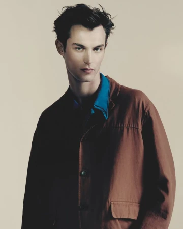 Model Kit Butler posing in a brown utility jacket and bright blue collared shirt against a neutral studio backdrop.