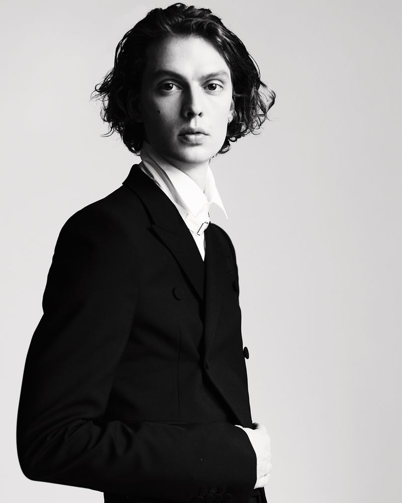 Monochrome studio portrait of model Leon Dame wearing a black double-breasted suit jacket and white collared shirt.