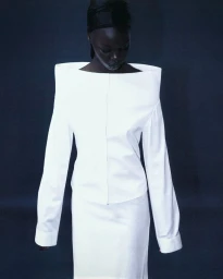 Model wearing a structured white off-the-shoulder top against a dark moody background for Bonnetje Spring Summer 2025.