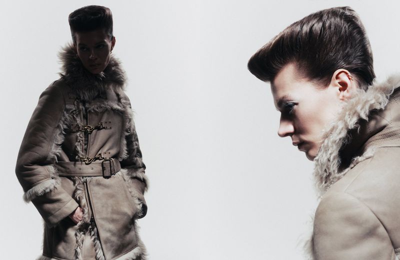 Fashion photography showcasing a person with a distinctive hairstyle and wearing a furry tan coat in a studio setting.