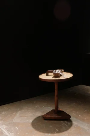 A wooden pedestal table with bowls and straps on top, lit by a spotlight against a dark background.