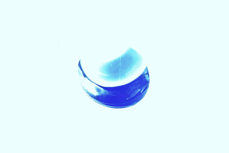 Abstract macro shot of a glass orb filled with blue liquid, set against a bright white background, emphasizing color contrast and texture.