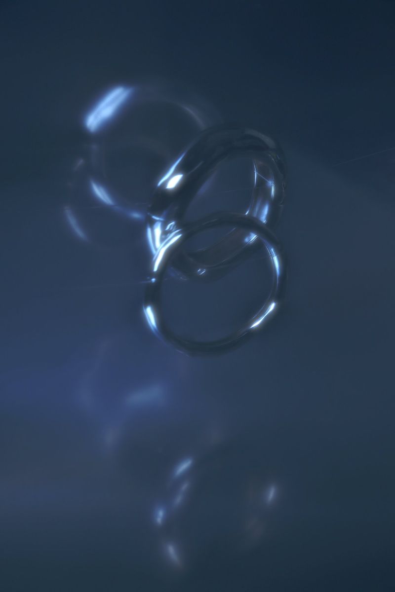 Abstract image of shiny, interlocked rings on a dark blue background with light reflections and highlights, creating a modern aesthetic.