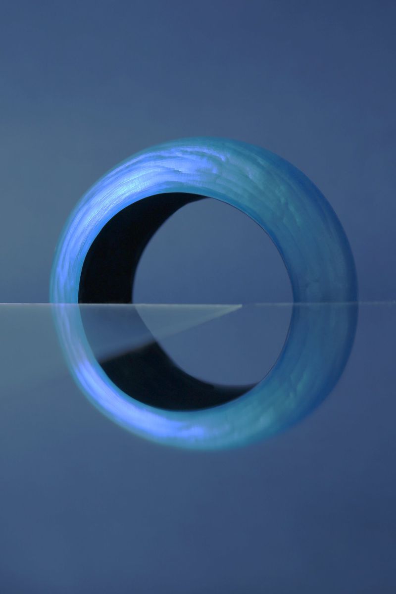 Close-up studio shot of a blue torus on a reflective surface, capturing its three-dimensional form and simple geometric design.