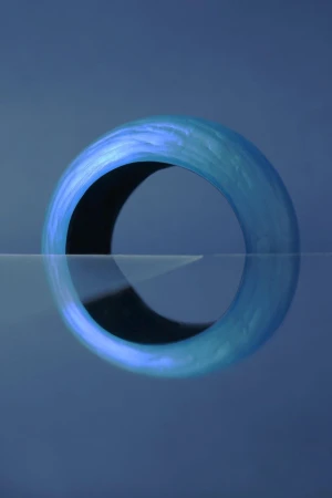 Close-up studio shot of a blue torus on a reflective surface, capturing its three-dimensional form and simple geometric design.